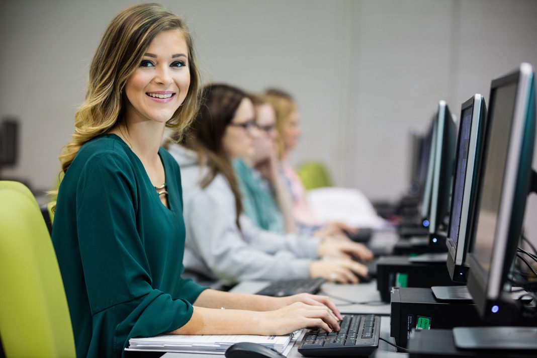 A student sits in a computer lab and looks directly at the camera
