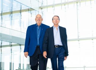 50 Years of Friendship Tech Alumni George Mitchell and Jack Dixon walk towards to the camera on a floor that reflects the confident blues of their suits