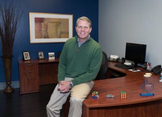 Alumni Stories: Brent Garrett Brent Garrett sits on the corner of a large wooden desk with his hands folded in his lap