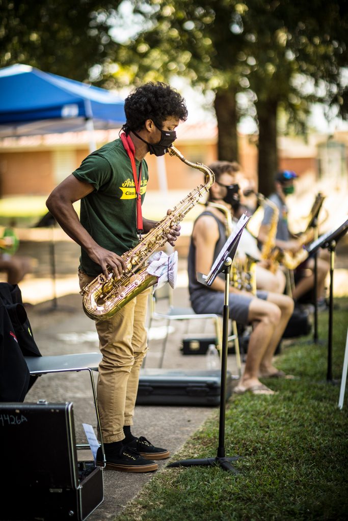 A tenor saxophone player stands to play a solo outdoors.